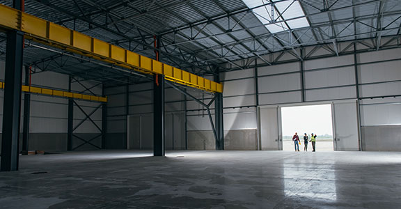 Architect team At Work Site With Blueprints standing at big hangar doors industrial building interior