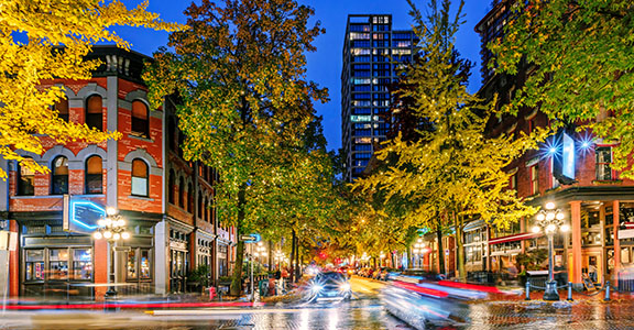 Night on the street in the old part of the big city with the lights of storefronts and shops, the blinding lights of car headlights and a paved roadway shimmering in neon lights after the last rain